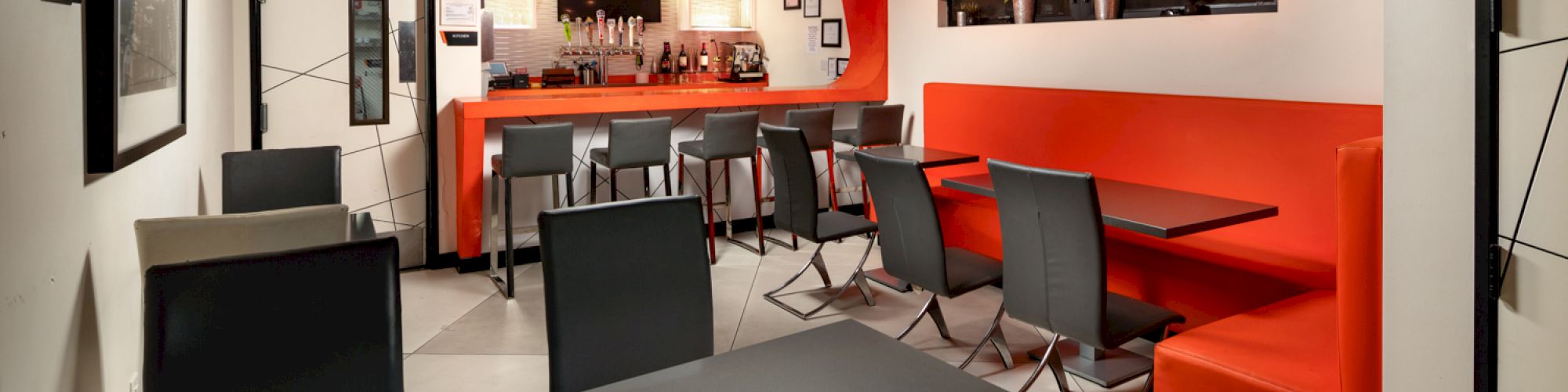 Modern cafe interior with orange walls, dark tables, and a bar area.