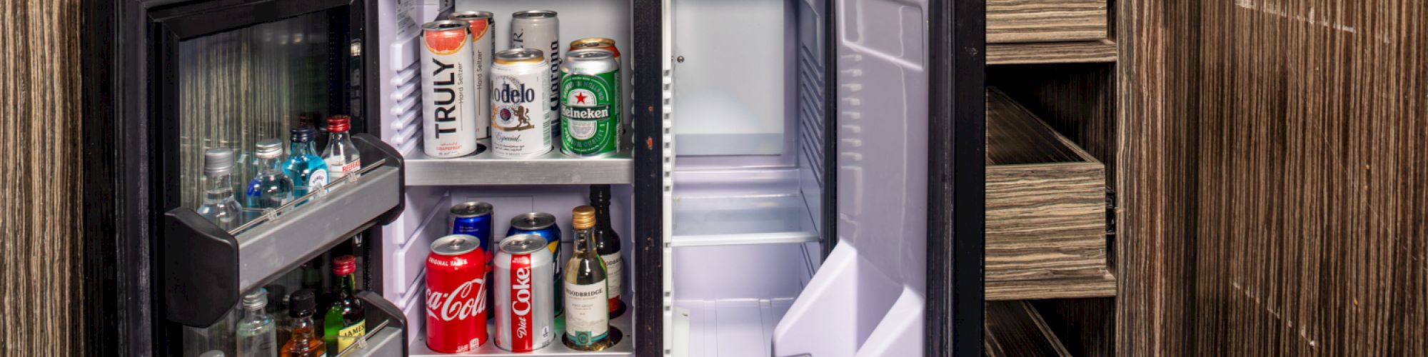 A mini fridge with various drinks inside is neatly tucked into a wooden cabinet.