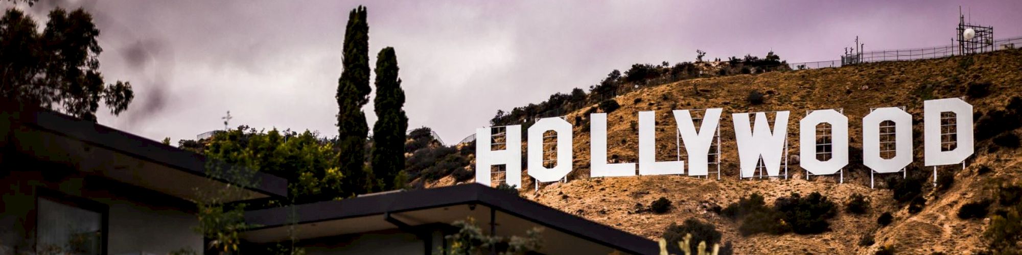 The famous Hollywood sign on a hill, dark clouds above, with foreground buildings.