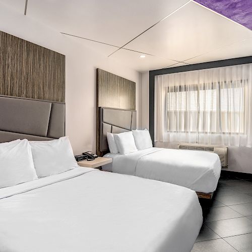 A modern hotel room with two beds, a TV, and a bright window.