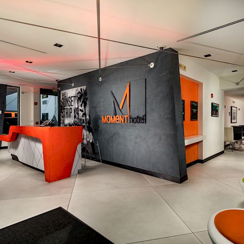 A stylish lobby or common area with modern decor, orange accents, artistic wall art, and various seating arrangements.