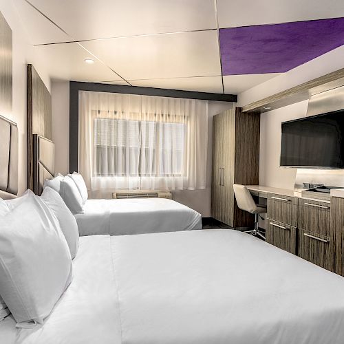 Modern hotel room with a double bed, white linens, a TV, and wooden furnishings.