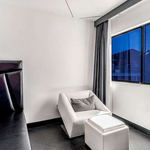 Modern room with a white sofa, ottoman, dark curtains, and a view through the window.