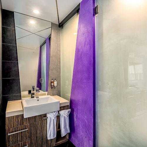 Modern bathroom with a white sink, mirror, purple accents, and frosted glass shower door.