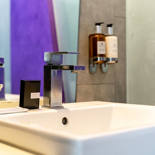 A modern bathroom sink with a sleek faucet, a soap dispenser, and two bottles mounted on the wall in the background.