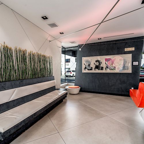 A modern interior with a long bench, wall art, plants, and an orange reception desk, located in a well-lit space with large windows.