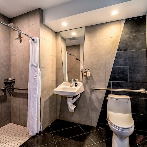 Modern bathroom with shower, toilet, and sink, tiled in grey tones.