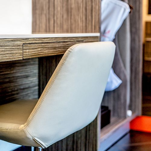 The image shows a beige chair tucked into a wooden desk with a drawer. In the background, there are cabinets and a red carpet strip.