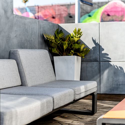 A modern outdoor seating area with a gray sofa, a rectangular coffee table, and a potted plant against a concrete wall.