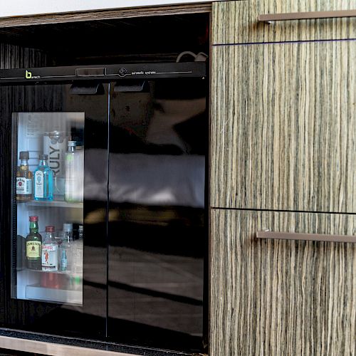 A mini fridge is built into a cabinet, with various small bottles of beverages visible through the glass doors.