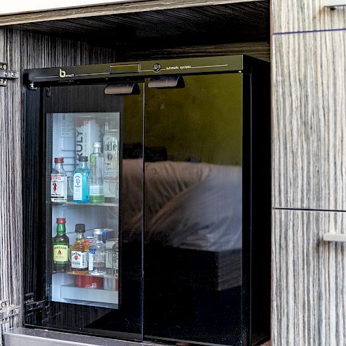 The image shows a small minibar or refrigerator built into a cabinet, containing various bottles of beverages, including alcohol and water.