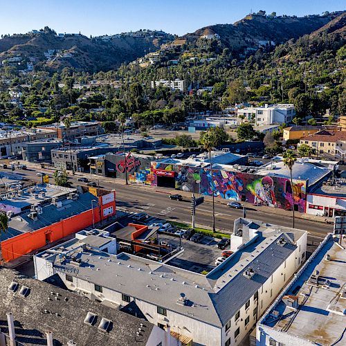 The image shows an aerial view of a colorful urban area with murals on buildings and a backdrop of green, hilly terrain.