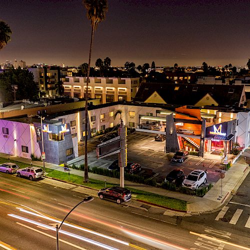 A nighttime view of an urban area with cars, buildings, streetlights, and a busy road with light trails from moving vehicles ending the sentence.