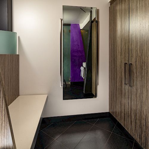 A modern interior with wooden cabinets, a wall mirror, and a seating area. There is a purple element visible in the mirror's reflection.