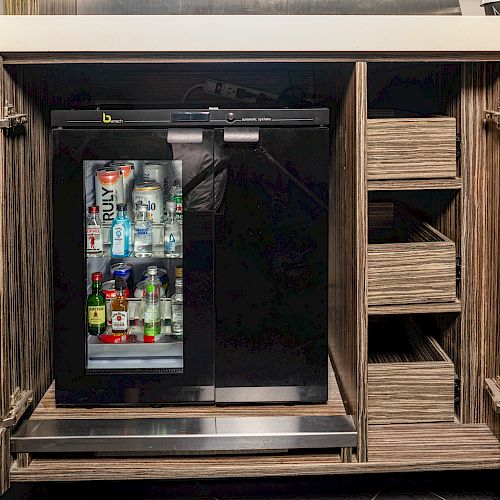 An open cabinet reveals a mini fridge stocked with drinks, alongside empty shelf spaces on the right.