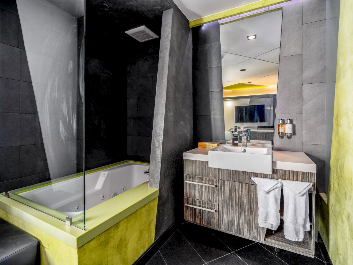 A modern bathroom with a bathtub, a sink with a mirror, and towels hanging on a rack. The design features grey and green accents.