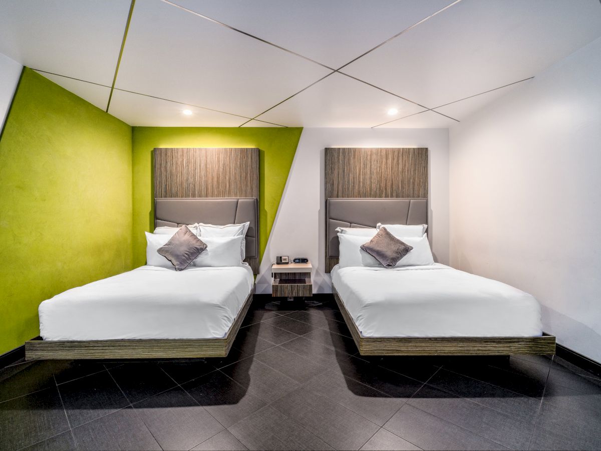 This image shows a modern bedroom with two single beds, accent walls in green, and an angled ceiling design, featuring minimalist decor.