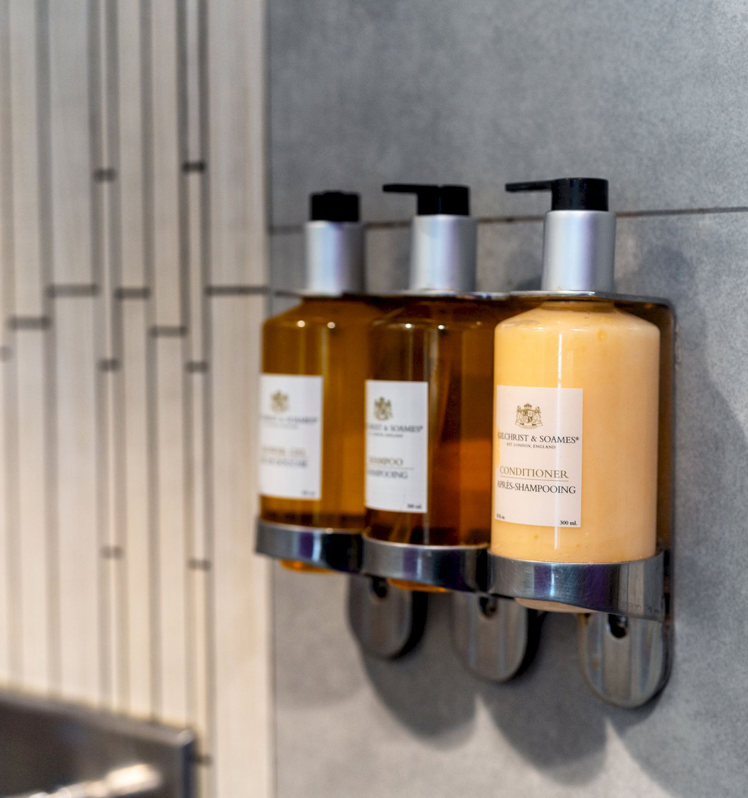 Three mounted liquid soap dispensers on a tiled wall.