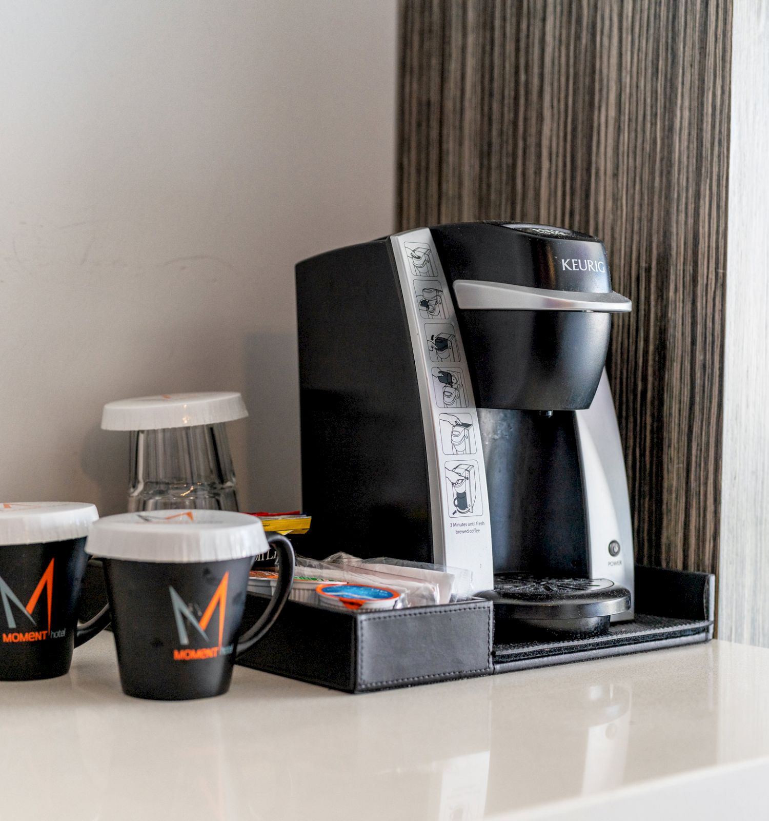 A coffee maker, two cups with logos, and coffee pods are on a kitchen counter.