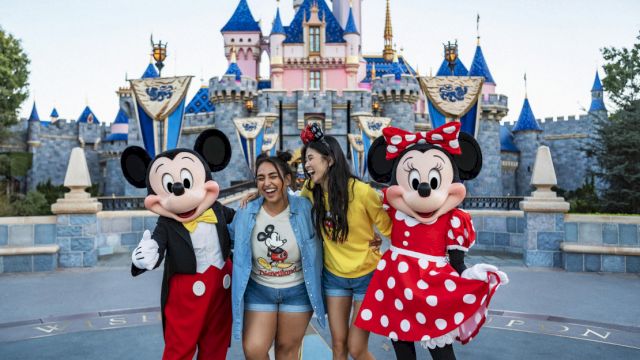 Two people pose with Mickey and Minnie Mouse in front of a castle at a Disney theme park, smiling and enjoying the moment.