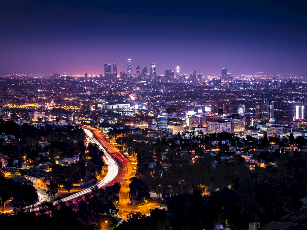 This image shows a night view of a city skyline with tall buildings and illuminated highways, creating a vibrant urban landscape.