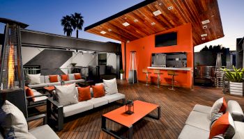 Cozy outdoor living space with modern furniture, fireplace, BBQ, under a wooden awning.