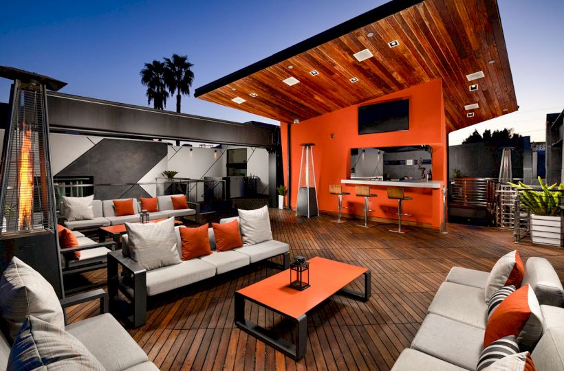 Cozy outdoor living space with modern furniture, fireplace, BBQ, under a wooden awning.