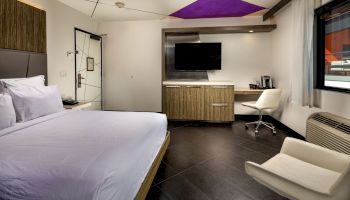 Modern hotel room with a bed, desk, chair, TV, and stylish decor.