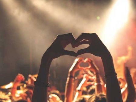 A crowd at a concert with a person forming a heart shape with their hands.